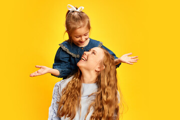 Little girl, daughter surprising her mother against yellow studio background. Celebrating women's holiday. Concept of Mother's Day, International Happiness Day, motherhood, childhood - obrazy, fototapety, plakaty