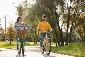 Beautiful young couple riding bicycles in park, space for text