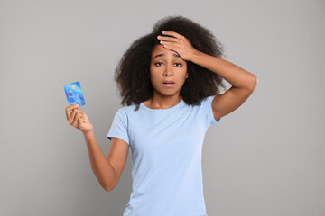 Confused woman with credit card on grey background. Debt problem