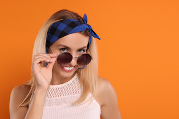 Portrait of smiling hippie woman in sunglasses on orange background. Space for text