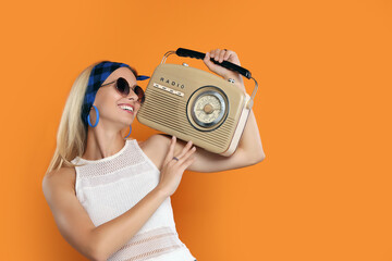 Happy hippie woman with retro radio receiver on orange background. Space for text
