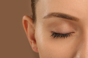 Woman with long eyelashes after mascara applying against light brown background, closeup
