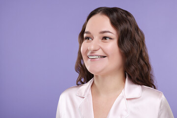 Fototapeta premium Smiling woman with dental braces on violet background, space for text