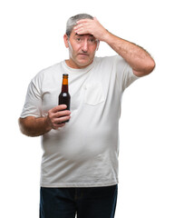 Handsome senior man drinking beer bottle over isolated background stressed with hand on head, shocked with shame and surprise face, angry and frustrated. Fear and upset for mistake.