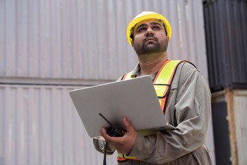 Portrait of male container yard worker loading containers box with laptop computer at commercial...