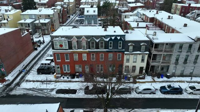 Snow-dusted rooftops of colorful townhouses on an urban street. Aerial establishing shot of snowy rowhouses.