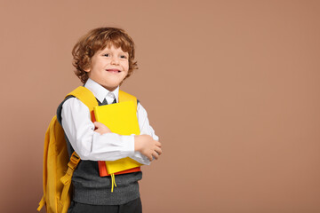 Happy schoolboy with backpack and books on brown background, space for text