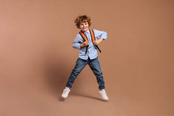 Happy schoolboy with backpack jumping on brown background