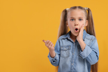 Special promotion. Emotional little girl pointing at something on orange background. Space for text