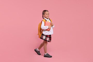 Happy schoolgirl with backpack and books on pink background