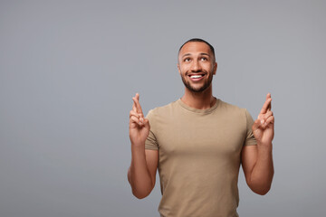 Happy man crossing his fingers on grey background, space for text