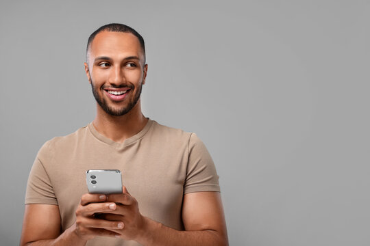 Happy man sending message via smartphone on grey background, space for text