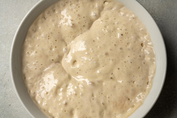 Top view sourdough starter in a bowl. Home baking, wild east, fermented food. - obrazy, fototapety, plakaty