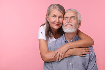 Portrait of happy affectionate senior couple on pink background, space for text