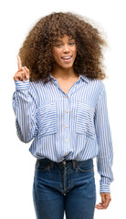 African american woman wearing a stripes shirt surprised with an idea or question pointing finger with happy face, number one