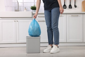 Woman taking garbage bag out of trash bin in kitchen, closeup