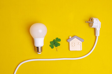 White LED light bulb, electric plug, leaf and a house symbol on yellow background. Concept of save...
