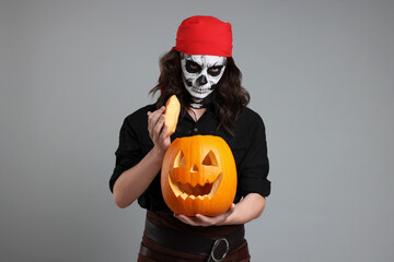 Man in scary pirate costume with skull makeup and carved pumpkin on light grey background....