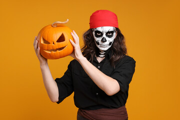 Man in scary pirate costume with skull makeup and carved pumpkin on orange background. Halloween celebration