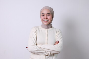 Smiling young beautiful Asian Muslim woman with braces standing with folded hands and looking at...