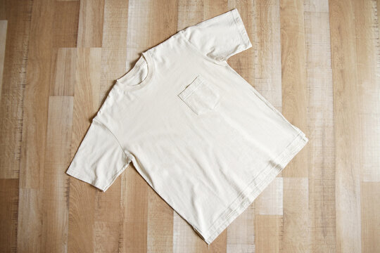Cream t-shirt with pocket front side on wooden background. 