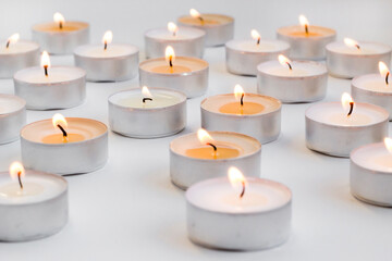 Many small round candles,tealight burns on a white background,conceptual image
