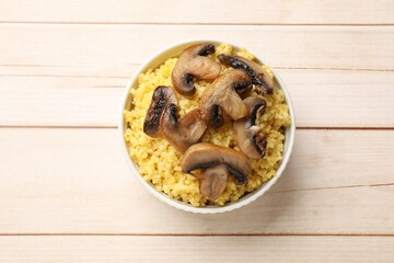 Tasty millet porridge and mushrooms in bowl on light wooden table, top view