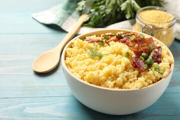 Tasty millet porridge with bacon, green onion and dill in bowl on light blue wooden table, closeup. Space for text