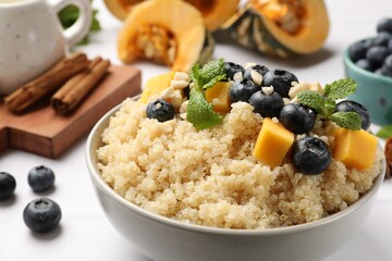 Tasty quinoa porridge with blueberries, pumpkin and mint in bowl on white table, closeup