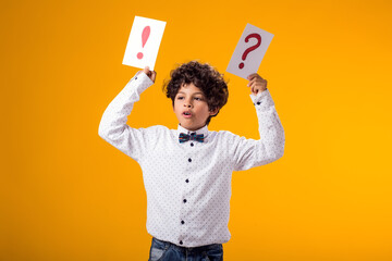 Child boy holding question mark and exclamation point cards. Brainstorming and choice concept