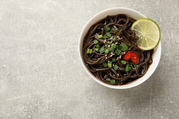 Tasty buckwheat noodles (soba) with sauce, onion and lime in bowl on light grey table, top view. Space for text