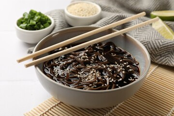 Tasty buckwheat noodles (soba) with sauce in bowl and chopsticks on white table, closeup