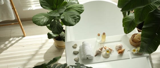 Bath tray with spa products, towels and shells on tub in bathroom, above view. Space for text