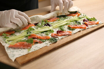 We wrap pita bread, forming a roll. Preparation of a roll with cheese, fish and vegetables
