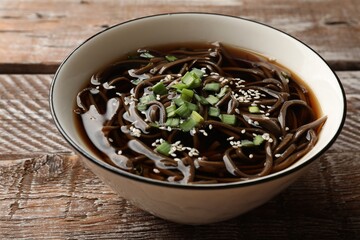 Tasty soup with buckwheat noodles (soba), onion and sesame in bowl on wooden table, closeup