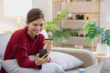 A young Asian woman with a happy smile holds a credit card and uses a smartphone to shop online Online payment concept.