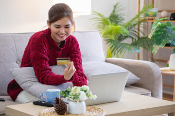 A young Asian woman with a happy smile holds a credit card and uses a smartphone to shop online Online payment concept.