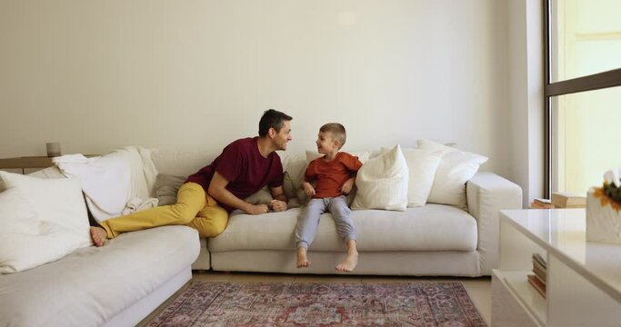 Active vivacious father and little 7s son have fun, play together in living room, catching up, running and flopped down, jumping on comfortable sofa, enjoy playtime on leisure. Games with kids at home