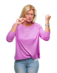 Middle age blonde woman eatin pink macaron biscuit over isolated background annoyed and frustrated shouting with anger, crazy and yelling with raised hand, anger concept