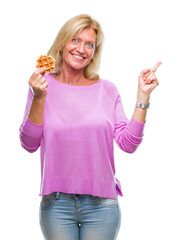 Middle age blonde woman eating sweet waffle over isolated background very happy pointing with hand and finger to the side