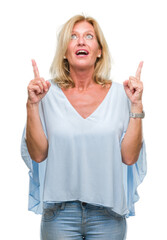 Middle age blonde business woman over isolated background amazed and surprised looking up and pointing with fingers and raised arms.