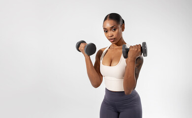 african american lady holds dumbbells works out against white backdrop