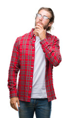 Young handsome man with long hair wearing glasses over isolated background with hand on chin thinking about question, pensive expression. Smiling with thoughtful face. Doubt concept.