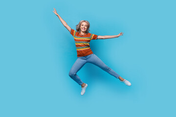 Obraz premium Full length photo of excited cheerful girl dressed print shirt jumping high arms sides isolated blue color background