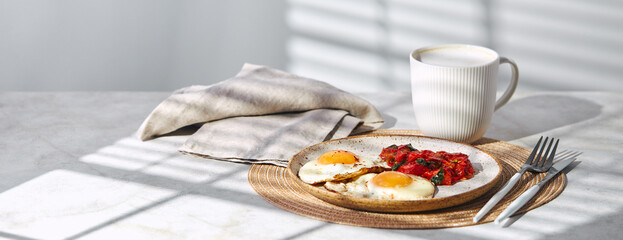 Breakfast with fried eggs and fried tomatoes with spinach on plate and cup of latte coffee