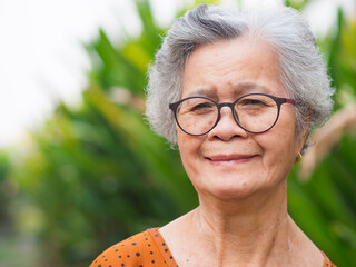 Portrait of an elderly Asian woman looking at the camera with a smile while standing in the garden.