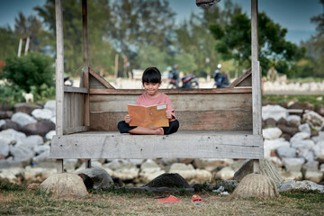 A cute little girl reading a book at a wooden gazebo outdoors