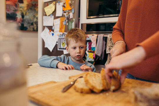Boy waiting at kitchen bench while parent slices bread
