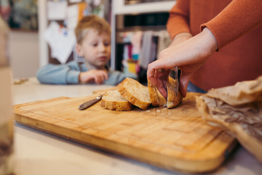 Boy waiting at kitchen bench while parent slices bread
