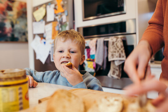 Boy eating bread while parent slices loaf